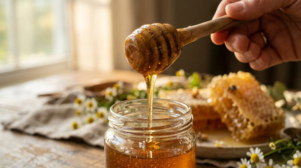 Golden honey dripping from a wooden dipper into a glass jar with honeycomb, representing natural health benefits of honey